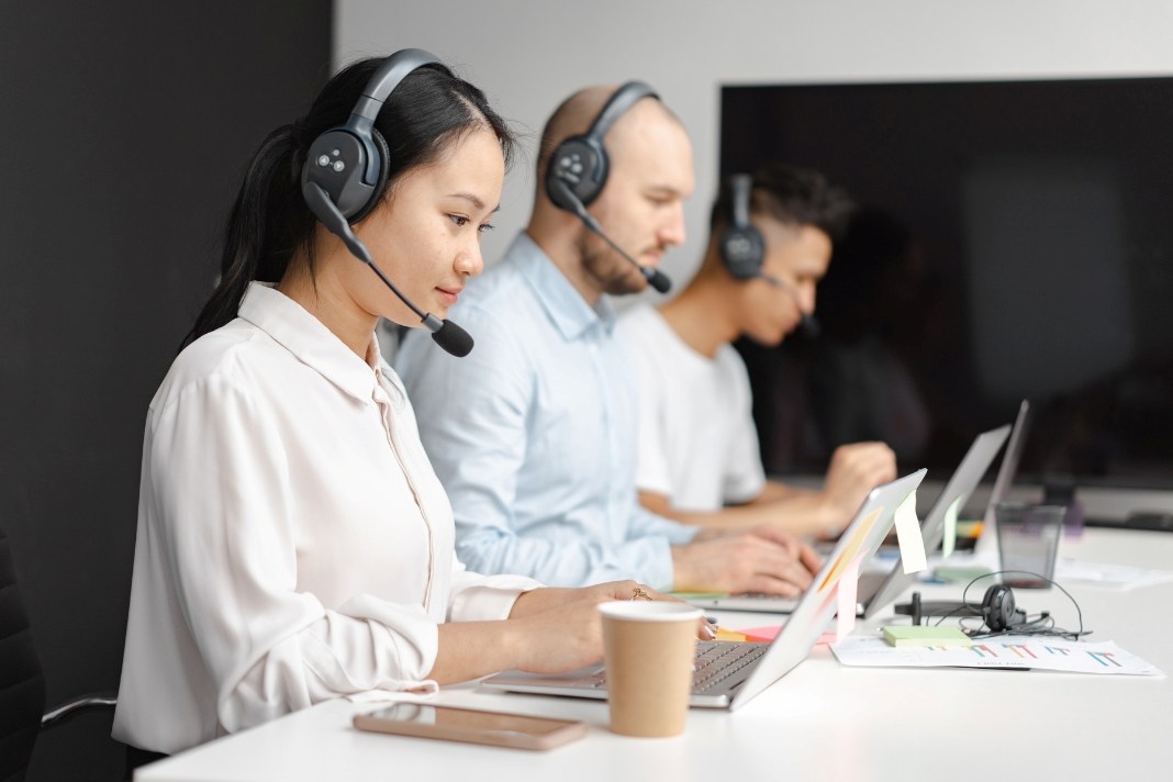 Customer support team wearing headsets and using laptops to help users contact ActivePropertyCare.com for property care service inquiries.