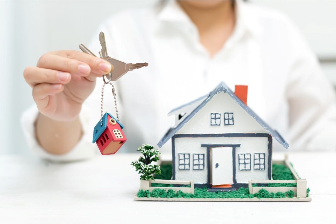 Person holding house keys beside a home model, showing ActivePropertyCare.com property care services for safer maintained homes.