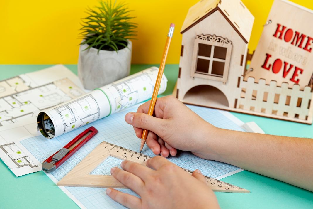 How To Guides ActivePropertyCare image showing hands drawing a home plan with a pencil, ruler, floor plans, and a small house model.