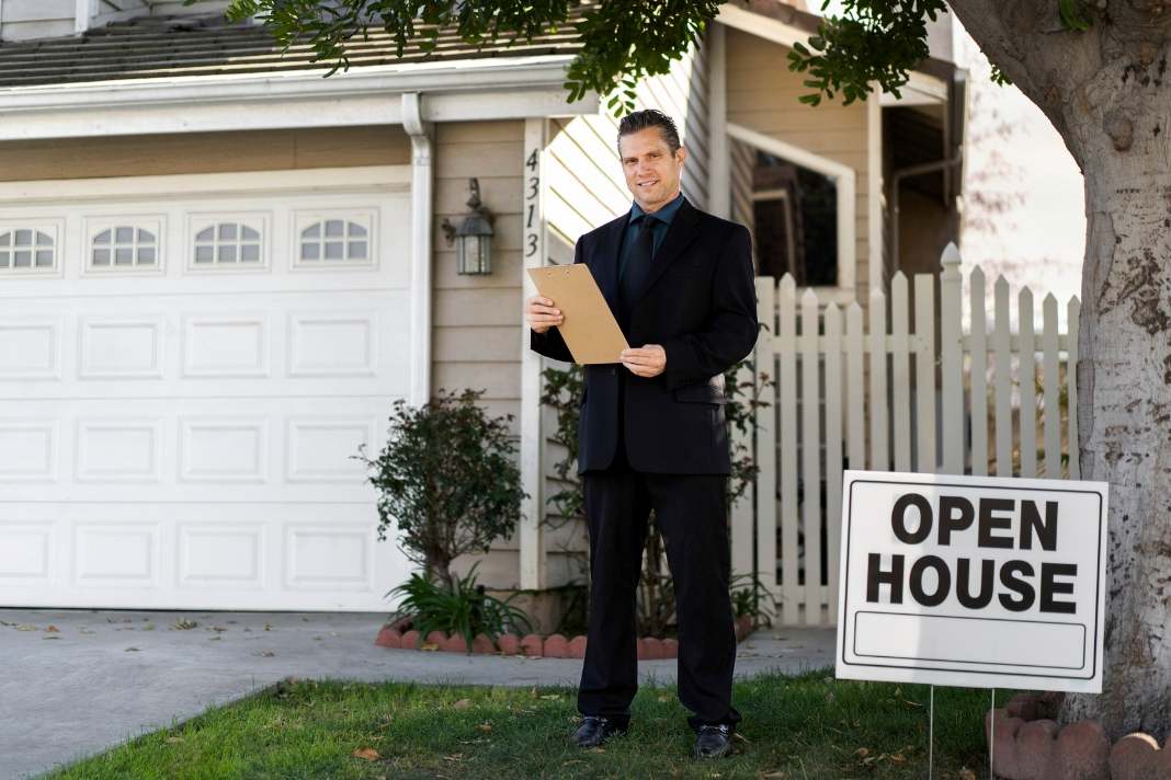 Real estate agent holding a clipboard outside a home with an open house sign, showing Berksaw ActivePropertyCare property guidance.
