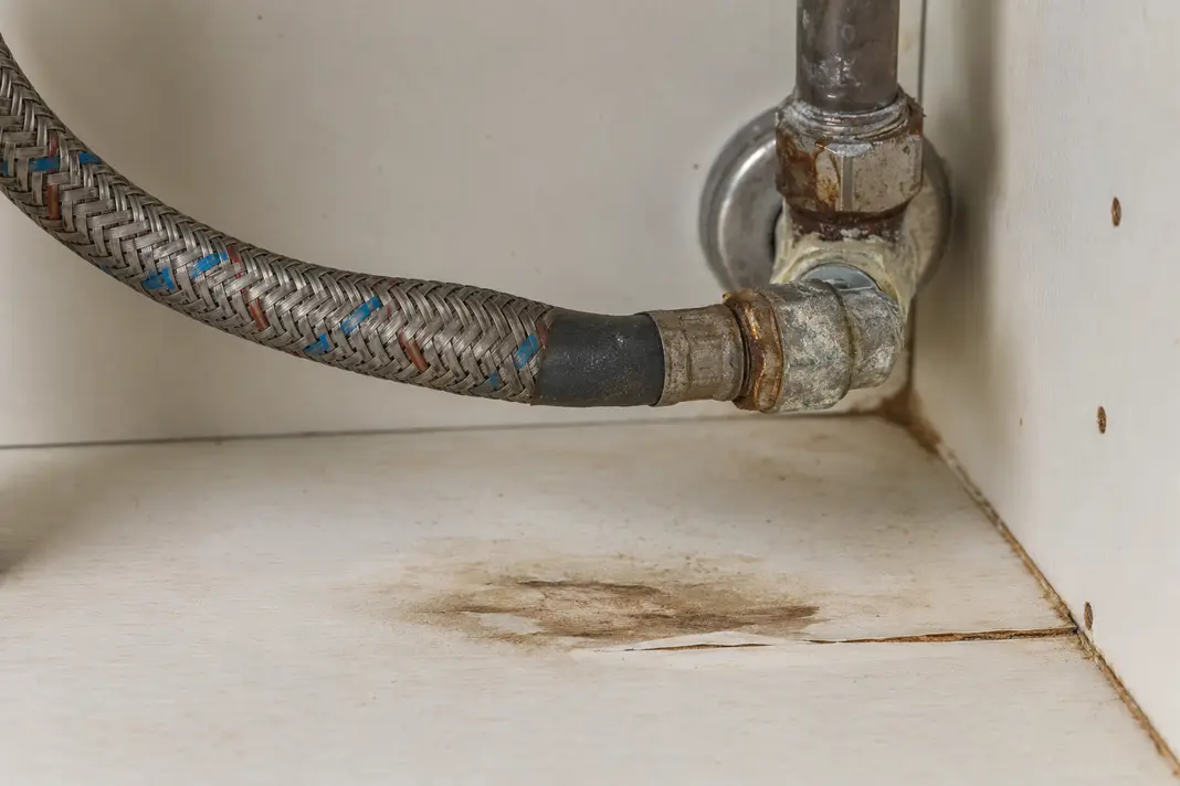 Corroded flexible hose showing damp and moisture warning signs inside a damaged cupboard