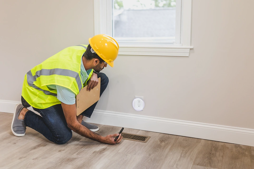 Property inspector verifying a floor vent and electrical outlet after repair work